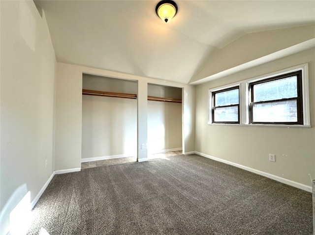 unfurnished bedroom featuring two closets, dark carpet, and vaulted ceiling