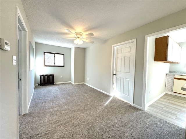 empty room featuring light carpet, a textured ceiling, radiator, and ceiling fan