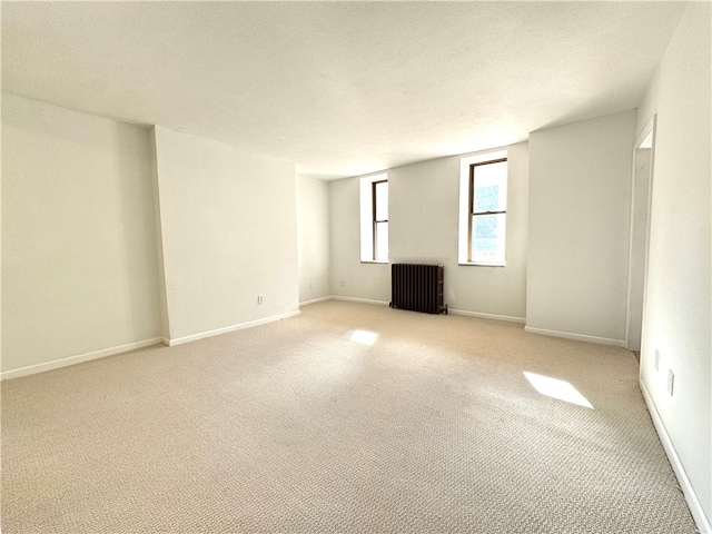 spare room featuring light colored carpet, radiator heating unit, and a textured ceiling