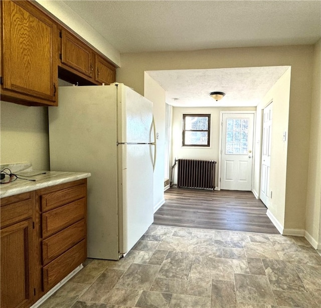 kitchen with radiator heating unit, white refrigerator, hardwood / wood-style flooring, and a textured ceiling