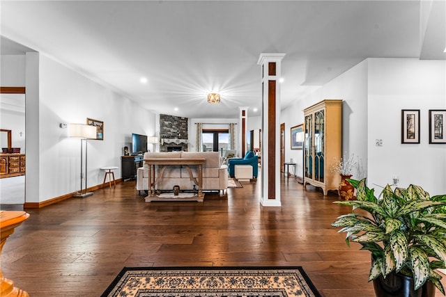 living room with decorative columns, a stone fireplace, and dark hardwood / wood-style floors