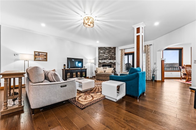 living room featuring a fireplace, ornate columns, and dark wood-type flooring