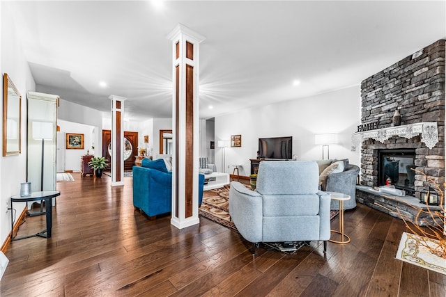 living room with a stone fireplace, dark hardwood / wood-style flooring, and ornate columns