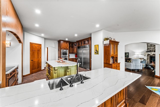 kitchen with sink, dark wood-type flooring, stainless steel appliances, a stone fireplace, and a kitchen island