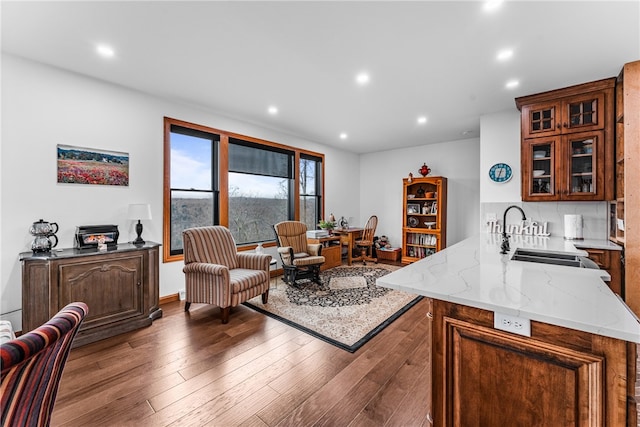 kitchen featuring kitchen peninsula, tasteful backsplash, light stone counters, sink, and wood-type flooring