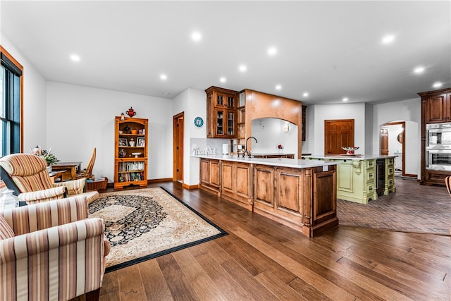 interior space featuring dark wood-type flooring, sink, double oven, a kitchen island, and kitchen peninsula