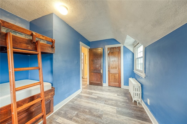 unfurnished bedroom featuring radiator heating unit, a textured ceiling, lofted ceiling, and hardwood / wood-style floors