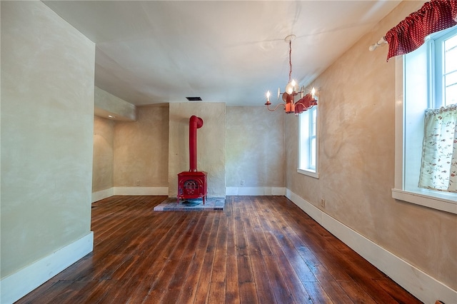 unfurnished living room with a wood stove, a wealth of natural light, dark wood-type flooring, and a notable chandelier