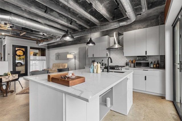 kitchen with tasteful backsplash, a kitchen island with sink, sink, wall chimney range hood, and pendant lighting