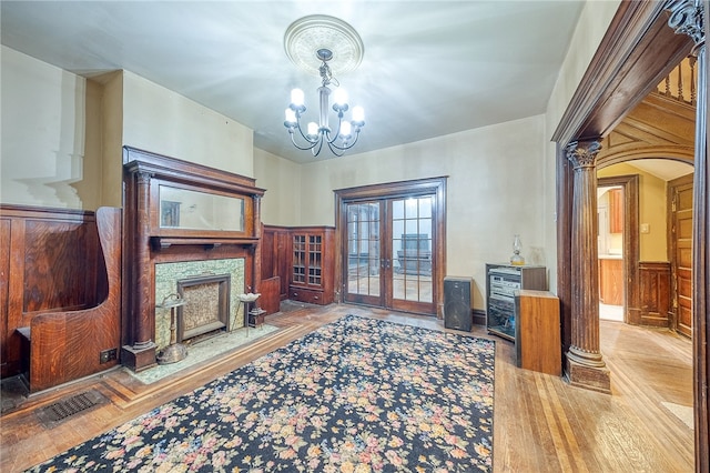 living room with french doors, a stone fireplace, wooden walls, a chandelier, and decorative columns