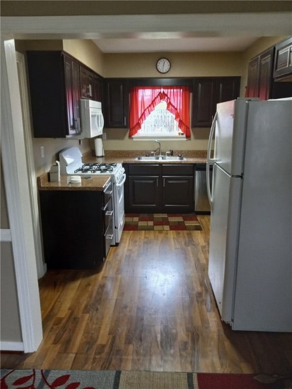 kitchen with dark brown cabinets, dark hardwood / wood-style flooring, white appliances, and sink