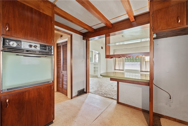 kitchen with beam ceiling, oven, and light colored carpet