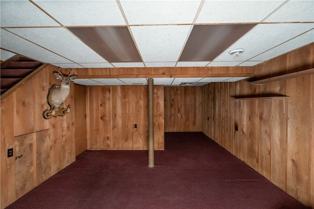 basement with wood walls, a drop ceiling, and dark carpet