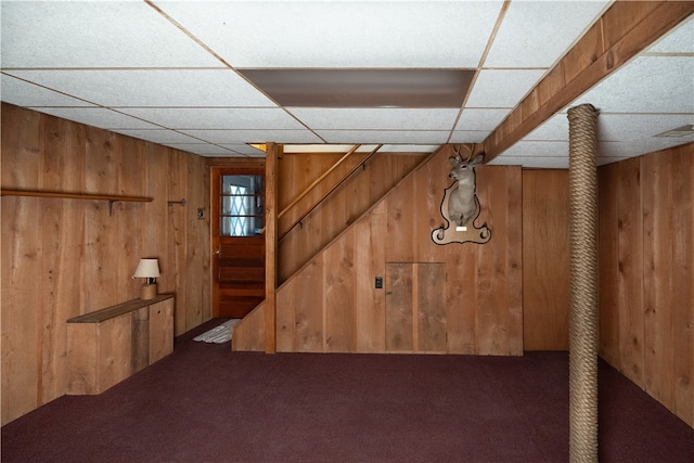 basement with a paneled ceiling, carpet flooring, and wooden walls