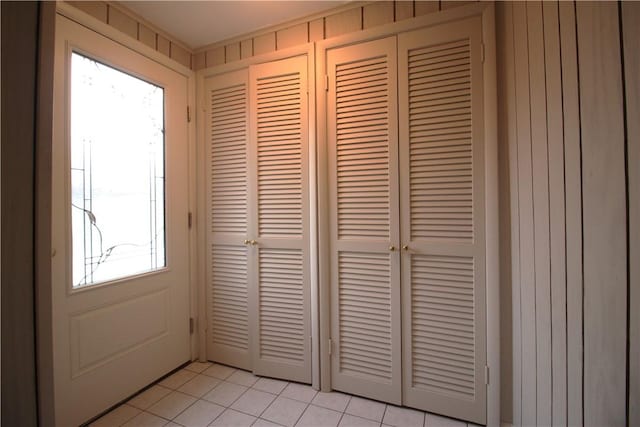 doorway to outside featuring light tile patterned floors, a healthy amount of sunlight, and wood walls