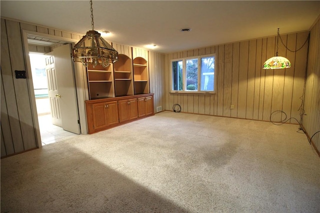 unfurnished living room featuring wood walls, light colored carpet, and an inviting chandelier