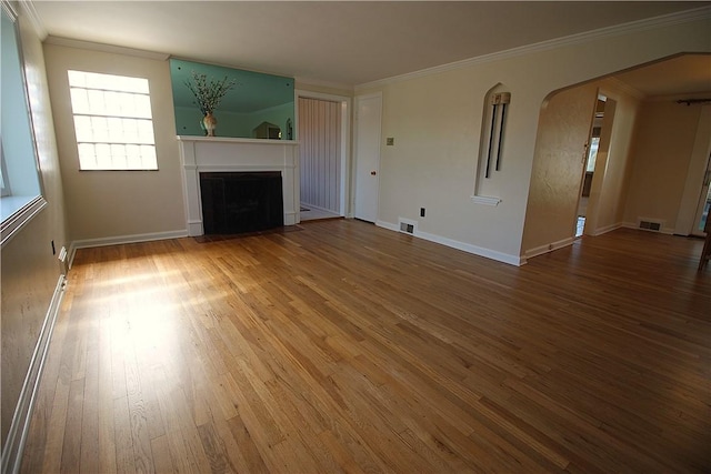 unfurnished living room with visible vents, arched walkways, wood-type flooring, a fireplace with flush hearth, and crown molding