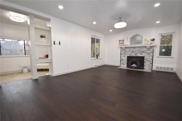 unfurnished living room featuring a healthy amount of sunlight, dark hardwood / wood-style flooring, and a wood stove