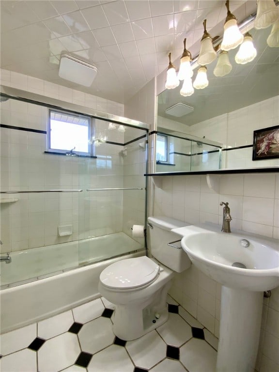 bathroom featuring tasteful backsplash, tile patterned floors, bath / shower combo with glass door, tile walls, and toilet