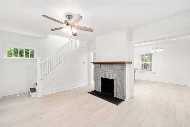 unfurnished living room with ceiling fan with notable chandelier, light wood-type flooring, a fireplace, and a wealth of natural light