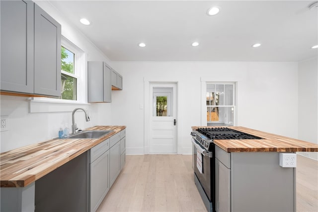 kitchen featuring wooden counters, light wood-type flooring, sink, gray cabinets, and stainless steel range with gas cooktop