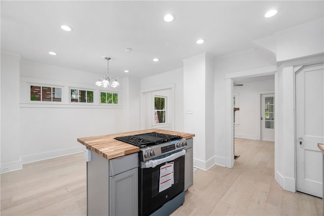 kitchen with gray cabinetry, hanging light fixtures, stainless steel stove, butcher block countertops, and plenty of natural light