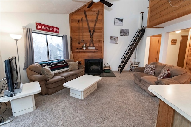 carpeted living room featuring wooden walls, a wood stove, ceiling fan, and lofted ceiling