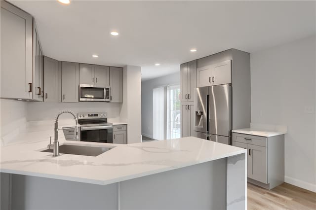 kitchen featuring sink, light hardwood / wood-style flooring, gray cabinets, kitchen peninsula, and stainless steel appliances