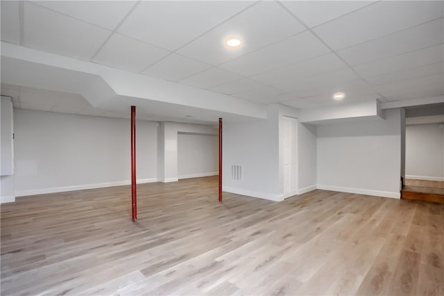 basement with a drop ceiling and light hardwood / wood-style flooring