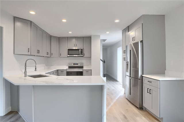 kitchen featuring kitchen peninsula, sink, light hardwood / wood-style flooring, and appliances with stainless steel finishes