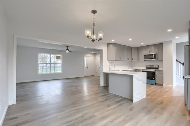 kitchen with gray cabinetry, hanging light fixtures, kitchen peninsula, appliances with stainless steel finishes, and light wood-type flooring