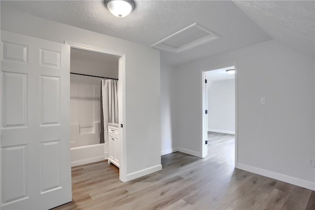 unfurnished bedroom featuring a textured ceiling, light wood-type flooring, ensuite bath, and vaulted ceiling