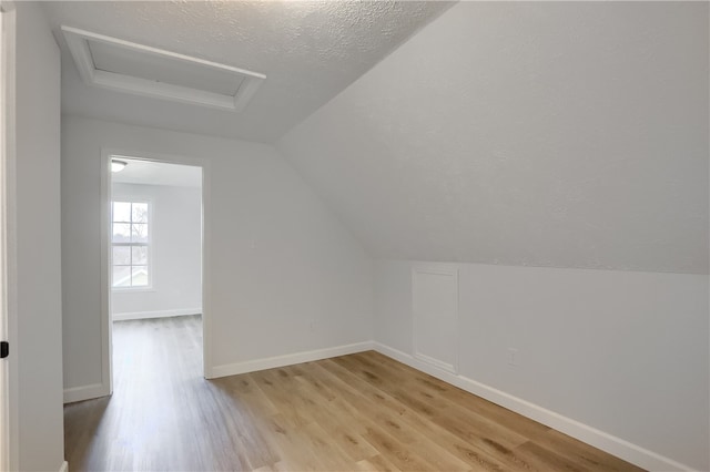 additional living space featuring a textured ceiling, vaulted ceiling, and light hardwood / wood-style flooring