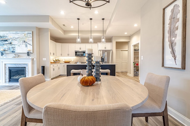 dining area featuring light hardwood / wood-style floors, a fireplace, and a tray ceiling