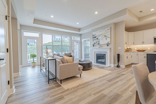 living room with light wood-type flooring, a high end fireplace, and a tray ceiling