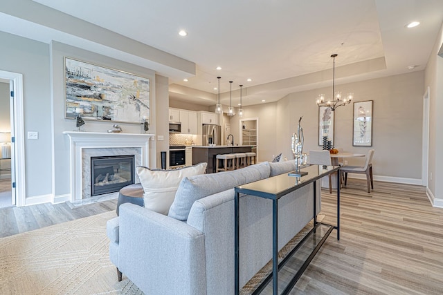 living room featuring a notable chandelier, light wood-type flooring, a high end fireplace, and a tray ceiling