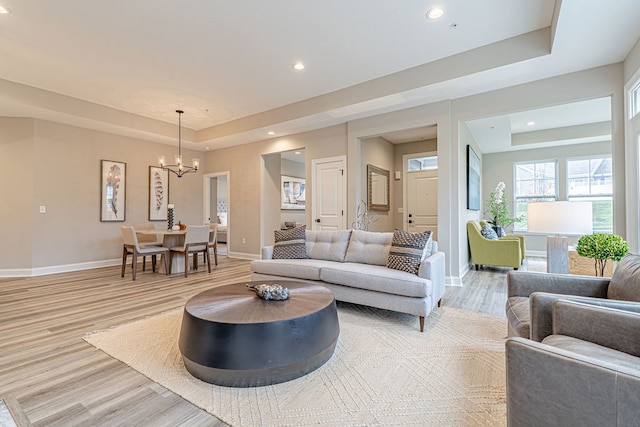 living room with a raised ceiling, light hardwood / wood-style floors, and an inviting chandelier