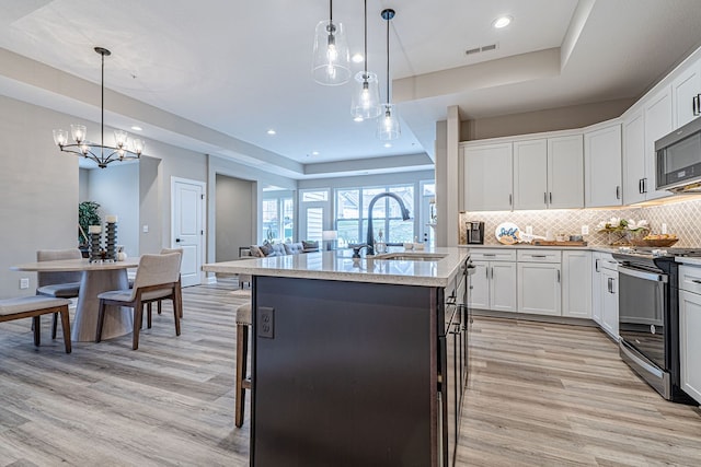 kitchen with appliances with stainless steel finishes, sink, a center island with sink, light hardwood / wood-style flooring, and hanging light fixtures