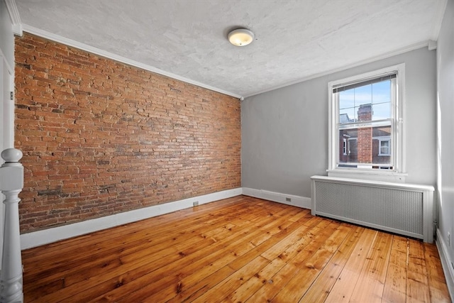 empty room featuring light wood-type flooring, radiator, crown molding, and brick wall