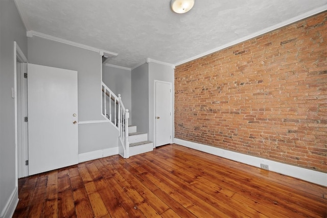 spare room featuring wood-type flooring, crown molding, and brick wall