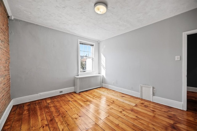 unfurnished room with crown molding, light hardwood / wood-style flooring, a textured ceiling, radiator heating unit, and brick wall