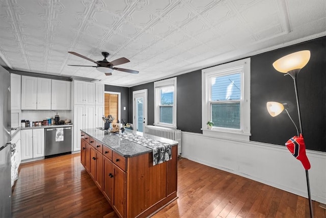 kitchen with light stone countertops, white cabinets, stainless steel dishwasher, and wood-type flooring