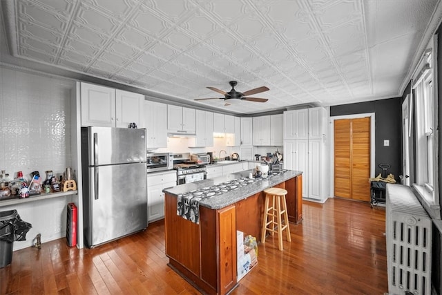 kitchen with white cabinets, stainless steel appliances, a kitchen island, and dark hardwood / wood-style floors