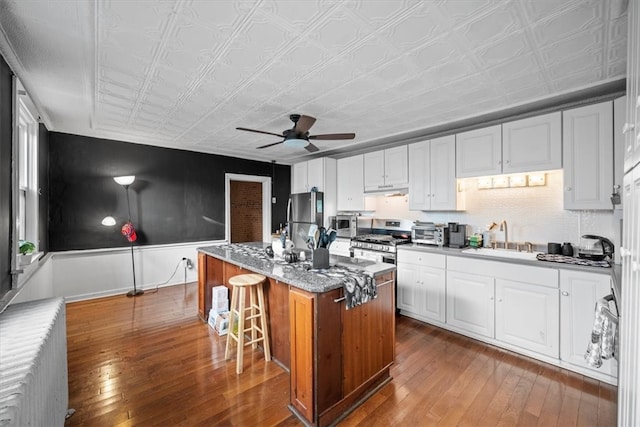 kitchen with white cabinetry, radiator heating unit, stainless steel appliances, a kitchen island, and hardwood / wood-style flooring