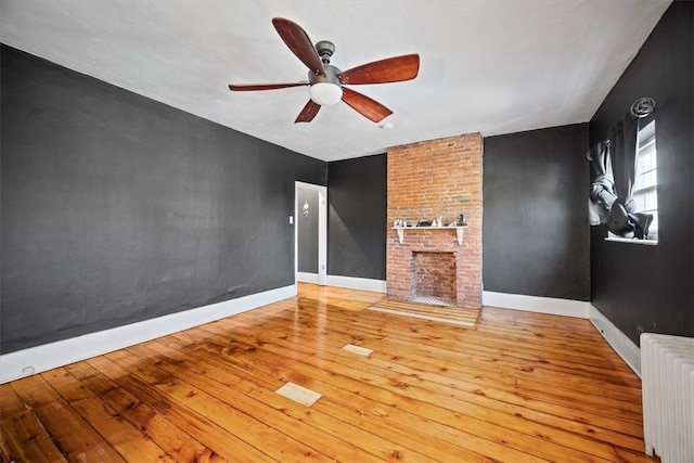 unfurnished living room with hardwood / wood-style floors, ceiling fan, radiator heating unit, and a fireplace