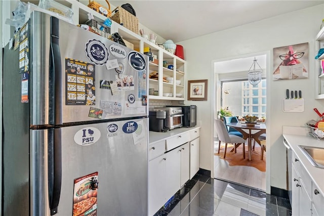 kitchen with white cabinets, sink, stainless steel fridge, dark tile patterned floors, and a notable chandelier