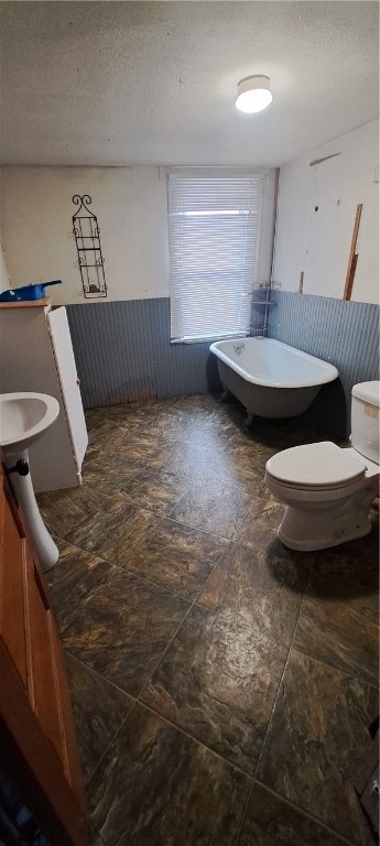 bathroom featuring a textured ceiling, a tub to relax in, and toilet