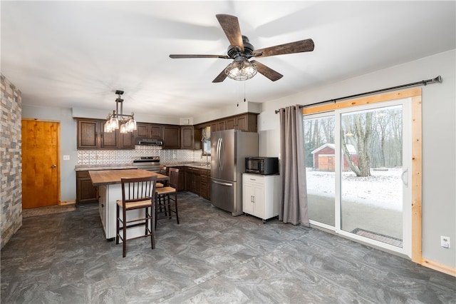 kitchen with appliances with stainless steel finishes, backsplash, dark brown cabinets, a kitchen island, and butcher block counters