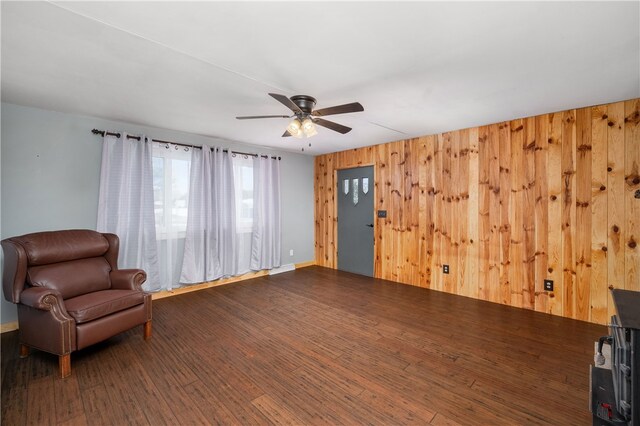 living area with ceiling fan, dark wood-type flooring, and wooden walls