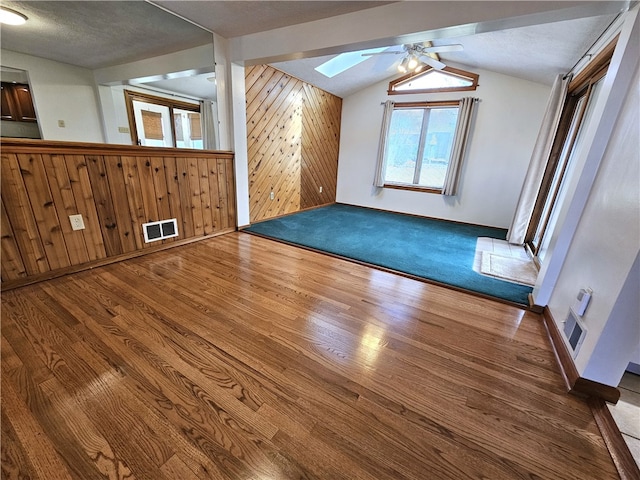 additional living space featuring wood-type flooring, a textured ceiling, lofted ceiling with skylight, and wood walls